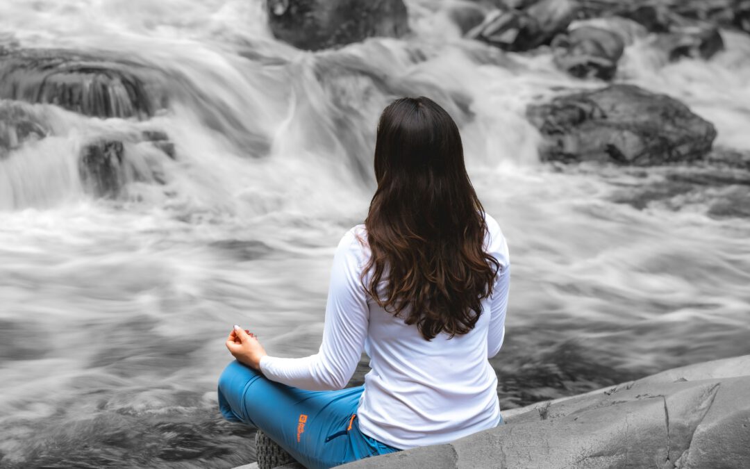 Een vrouw mediteert ontspannen voor een waterval, wat het belang van mindfulness van emoties illustreert voor herstel van verslaving